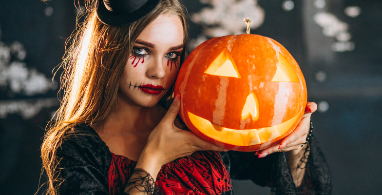 Halloween bulira beöltözött fiatal nő, aki egy faragott halloween tököt tart a kezében.