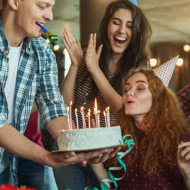 Vidám fiatal lány a születésnapi buliján éppen elfújja a tortáján a gyertyákat, a többiek ünneplik.